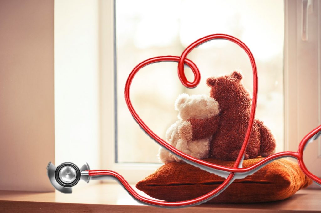 A white and brown bear hugging looking out of a window with a heart stethoscope